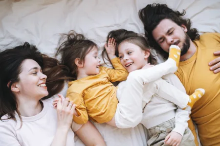 Young happy family with two children girls on bed at the cozy home, view from top